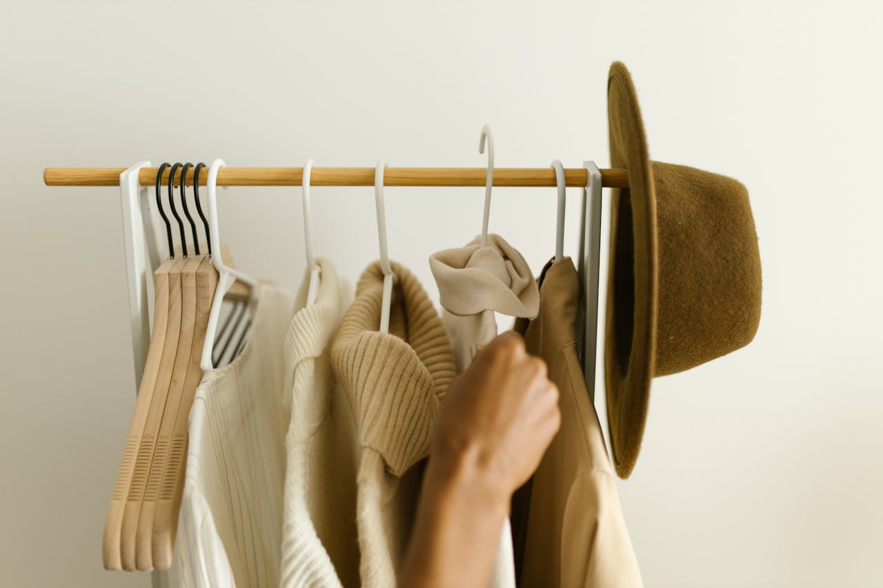 Stylish beige and brown clothes on a rack with a hand reaching in.